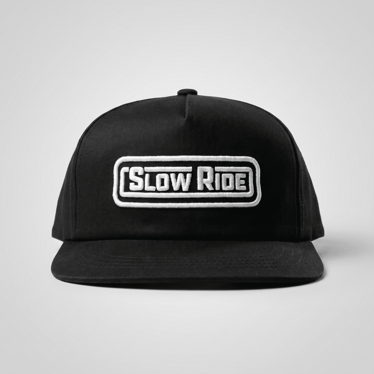 Radio Unstructured Snapback front view, Black with white embroidered "Slow Ride" text in rounded rectangular patch, Black