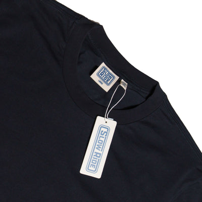 Care label on Road Trip Black Tee showing Cream-colored woven label with blue border and text on neckline, matching hang tag