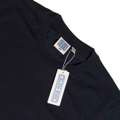 Care label on Road Trip Black Tee showing Cream-colored woven label with blue border and text on neckline, matching hang tag