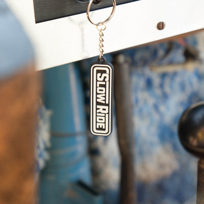 Radio Keychain - Slow Ride- Classic Slow Ride keychain featuring the iconic 'Slow Ride' logo in black and white, perfect for fans of Off-Roading and Off-Road Racing. This keychain is an ideal accessory for vintage Volkswagen enthusiasts, including those who love the Volkswagen bus, Volkswagen bug, and Baja bug. A great addition to any Garage and Racing lifestyle, this keychain embodies the spirit of Slow Ride Garage and mottos like 'Enjoy Getting There,' 'Wheelin and Spilling,' and 'Restore and Destroy.' A 